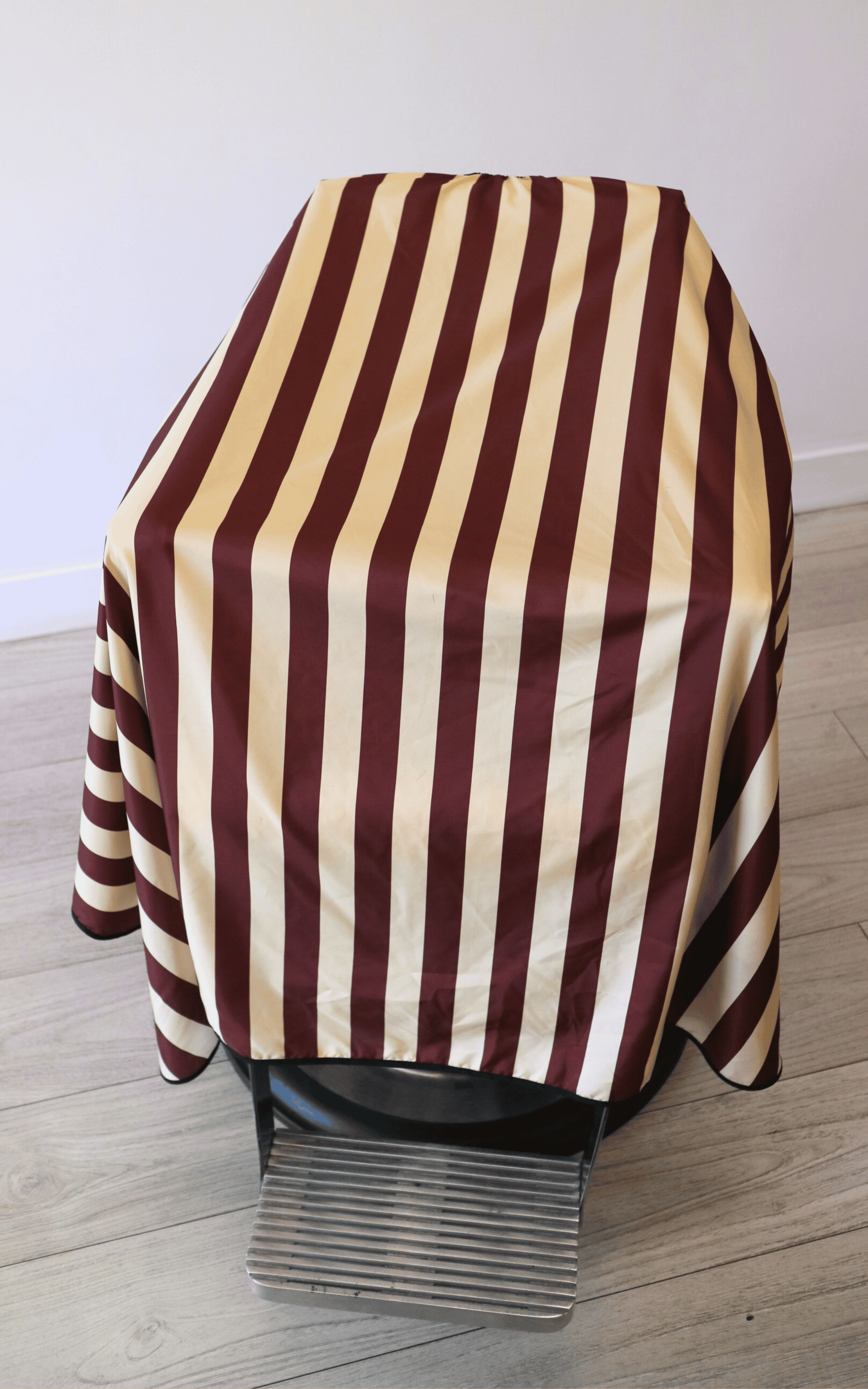 close up photo of burgundy and cream barber cape draped on barber chair