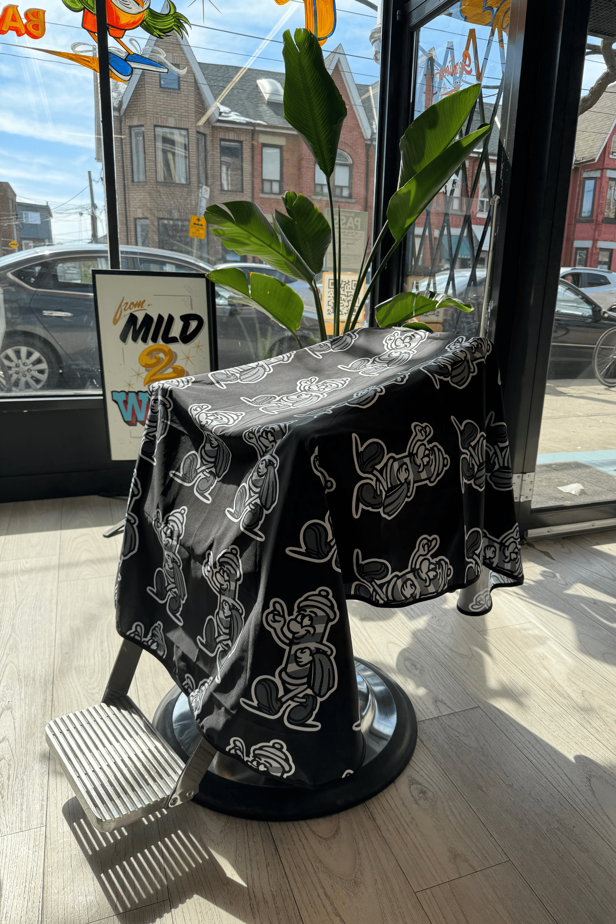 kids barber boy cutting cape inside barbershop and draped on barber chair with plant and sign in the background