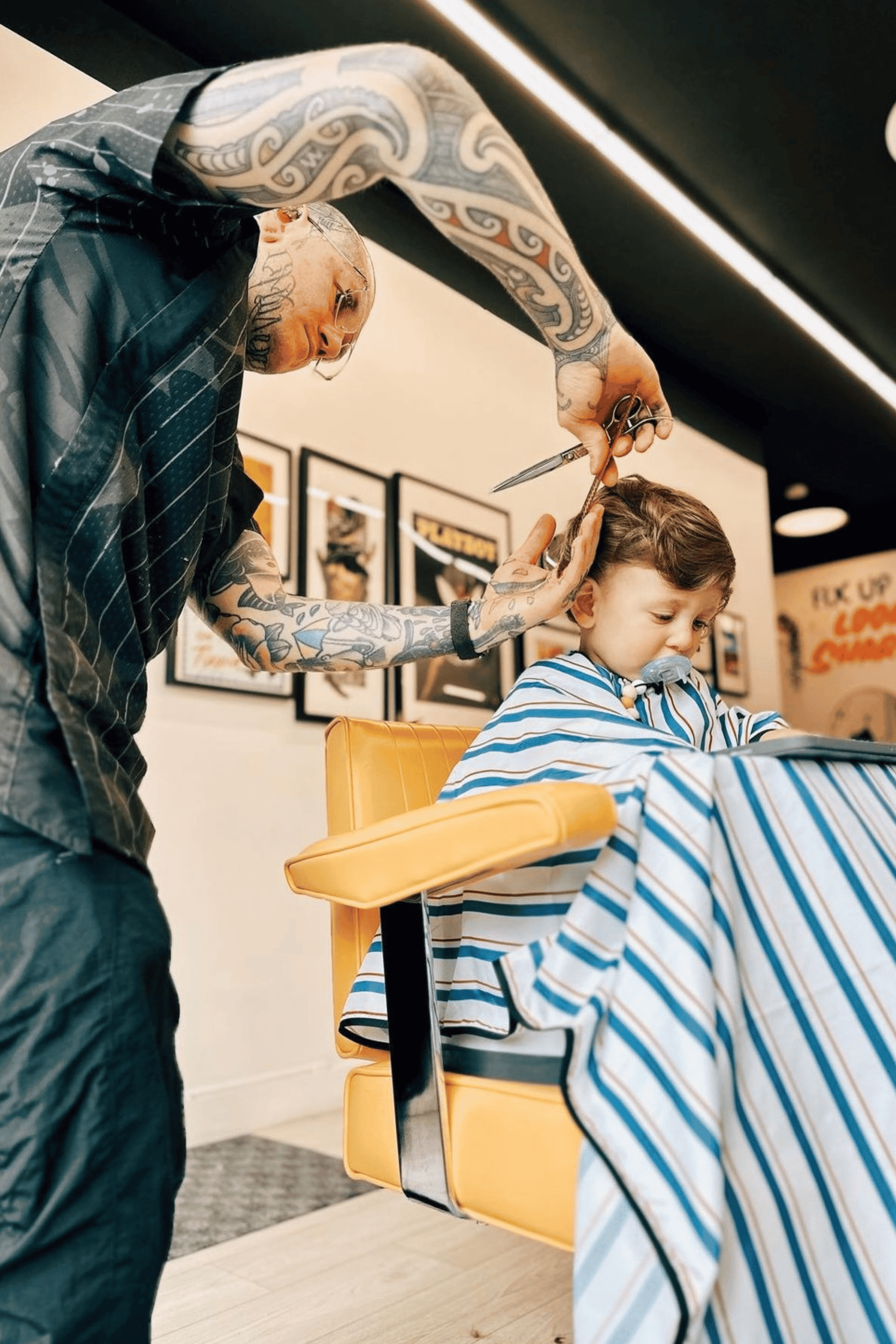 tattooed barber cutting kids hair in the blood and bandages kids cutting cape