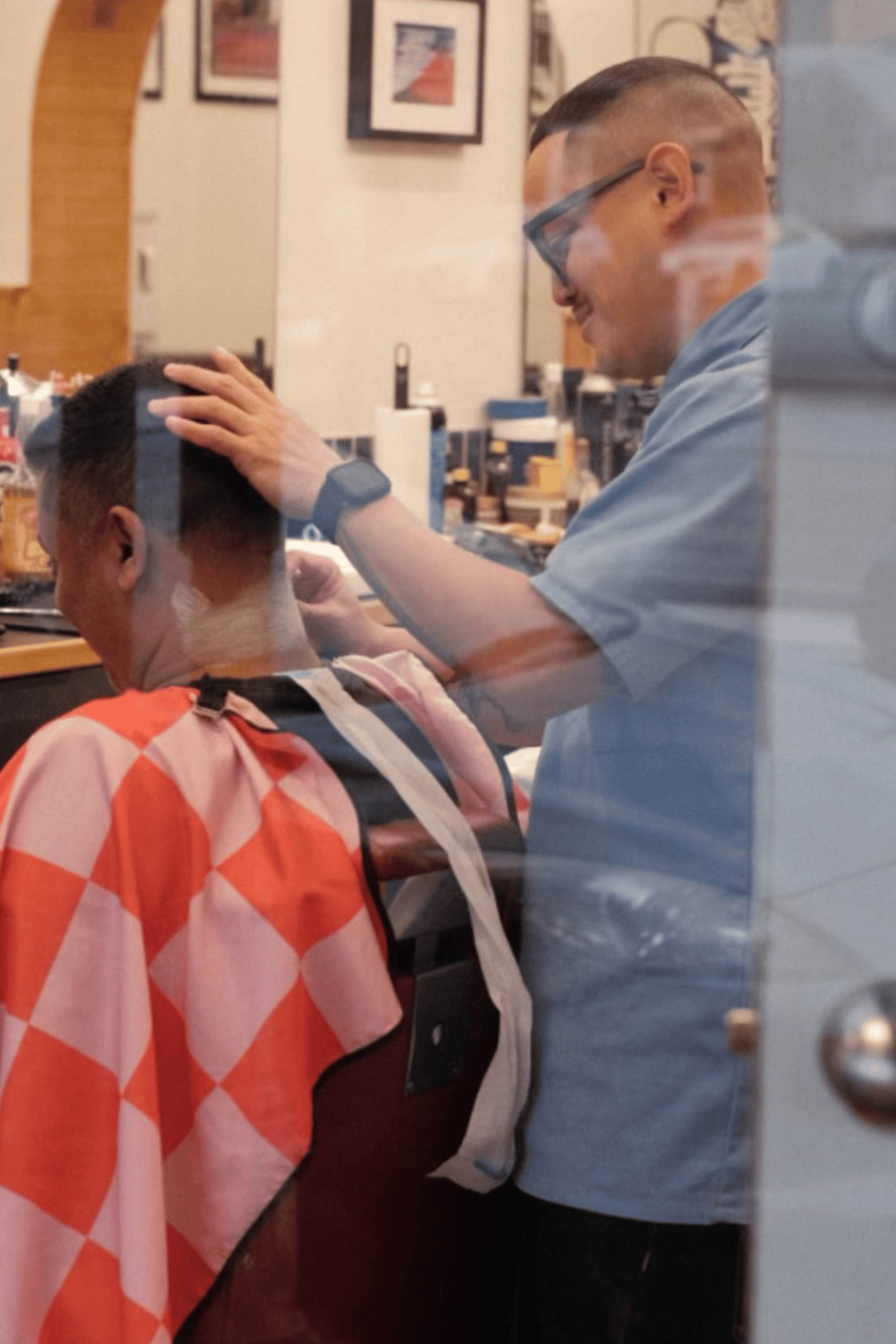 barber cutting customer hair using pink checker hair cutting cape