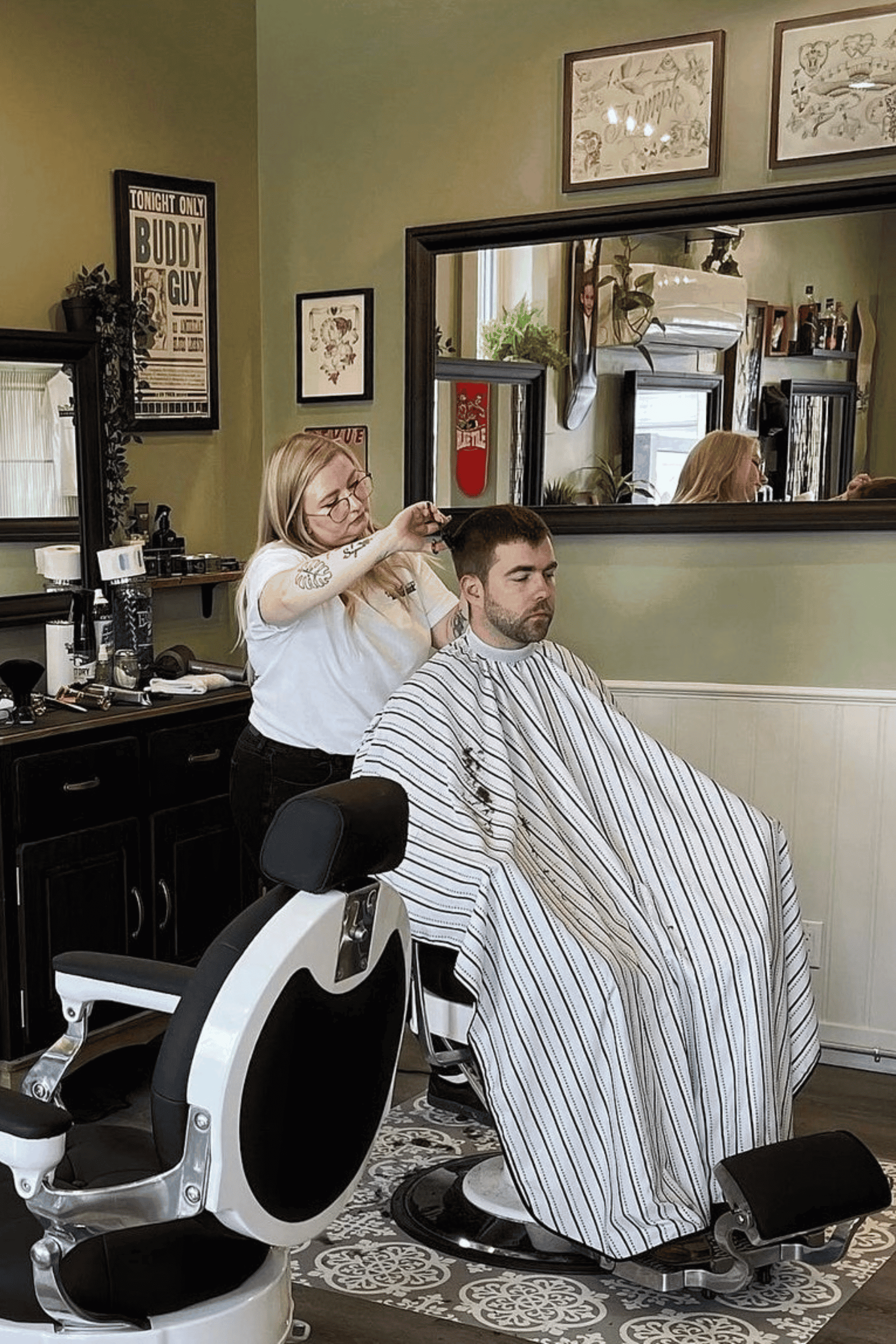 female barber cutting clients hair in modern pinstripe cape