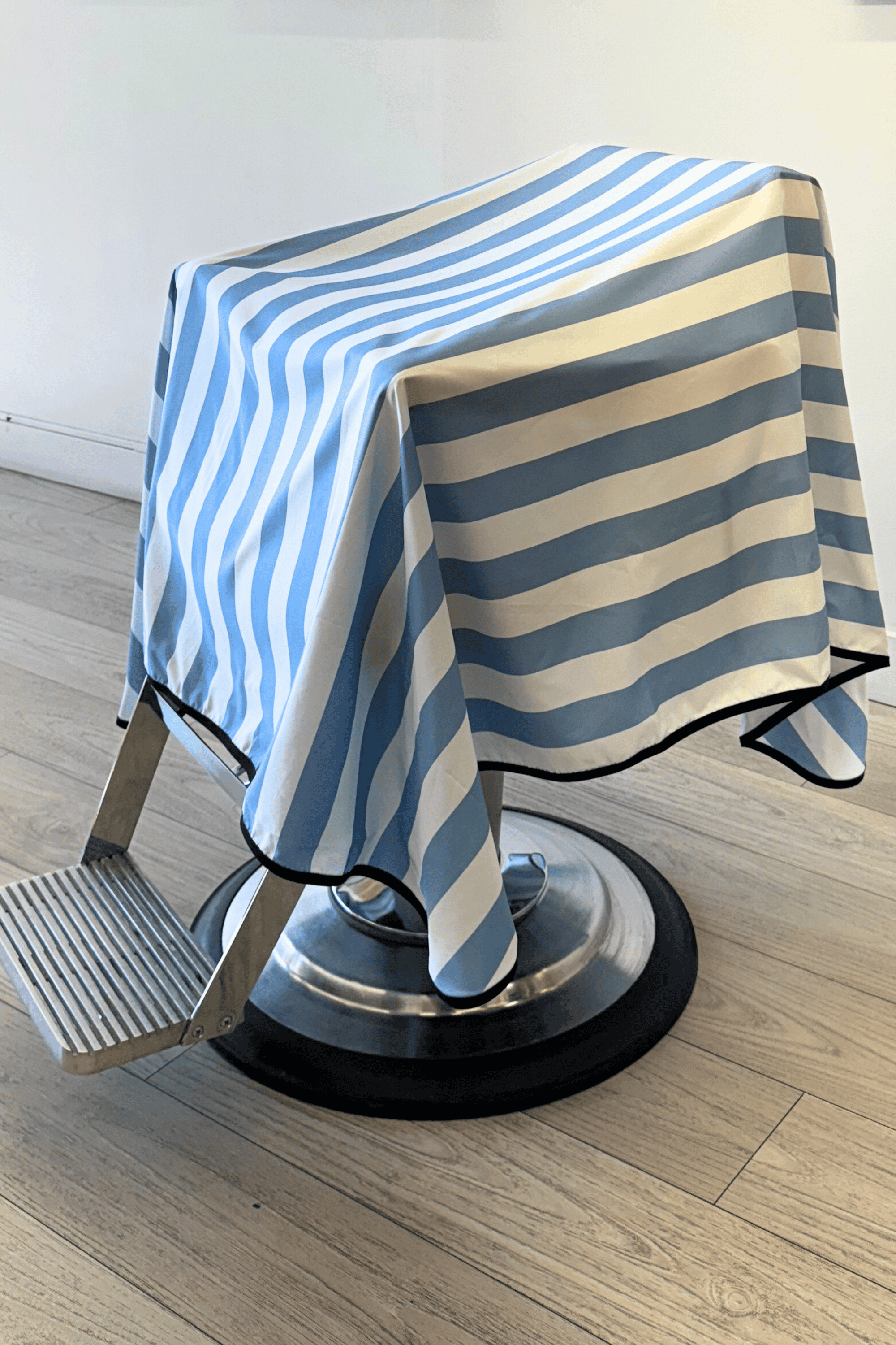 white and blue barber cape draped on barber chair