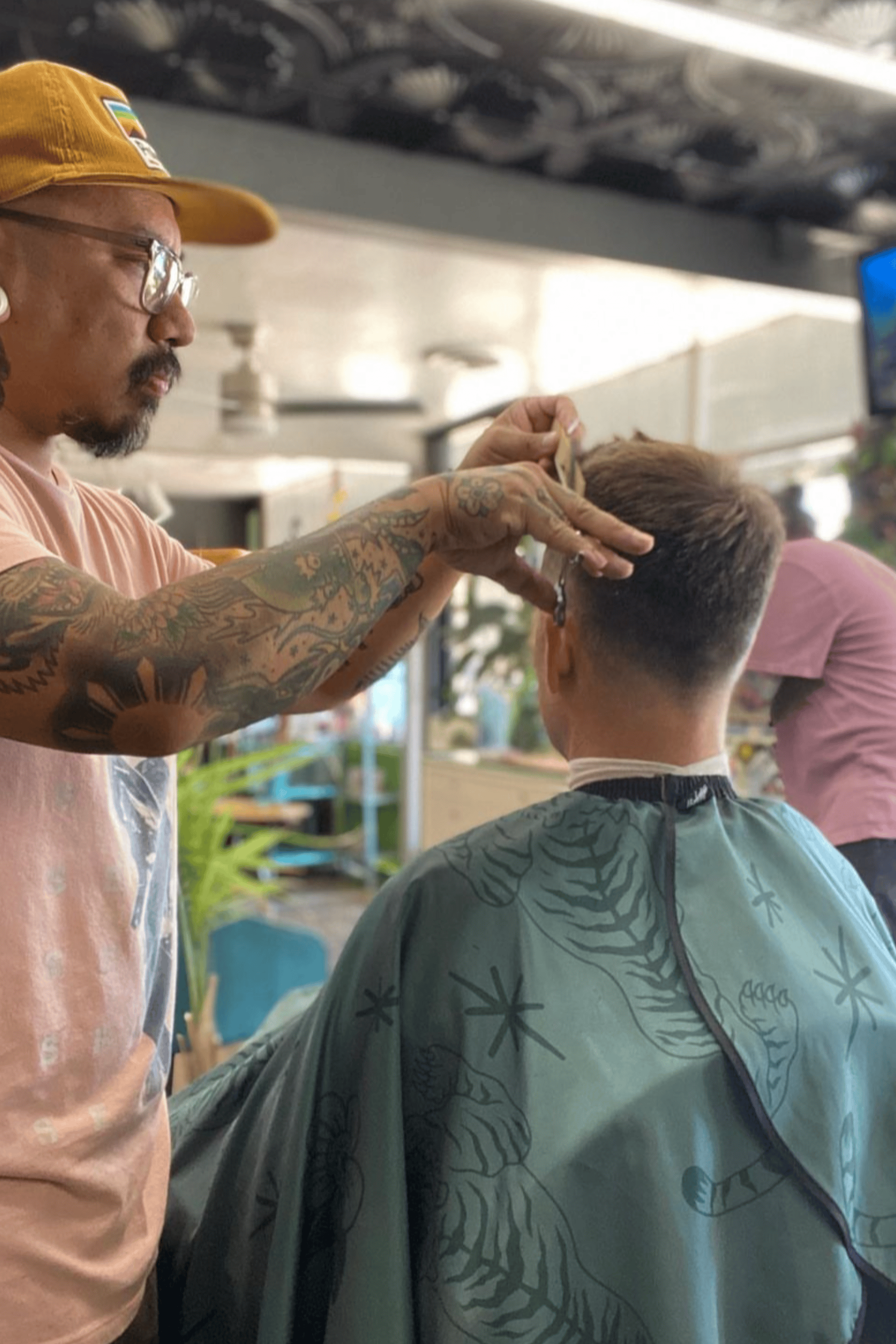 barber cutting customers hair using green tora cutting cape