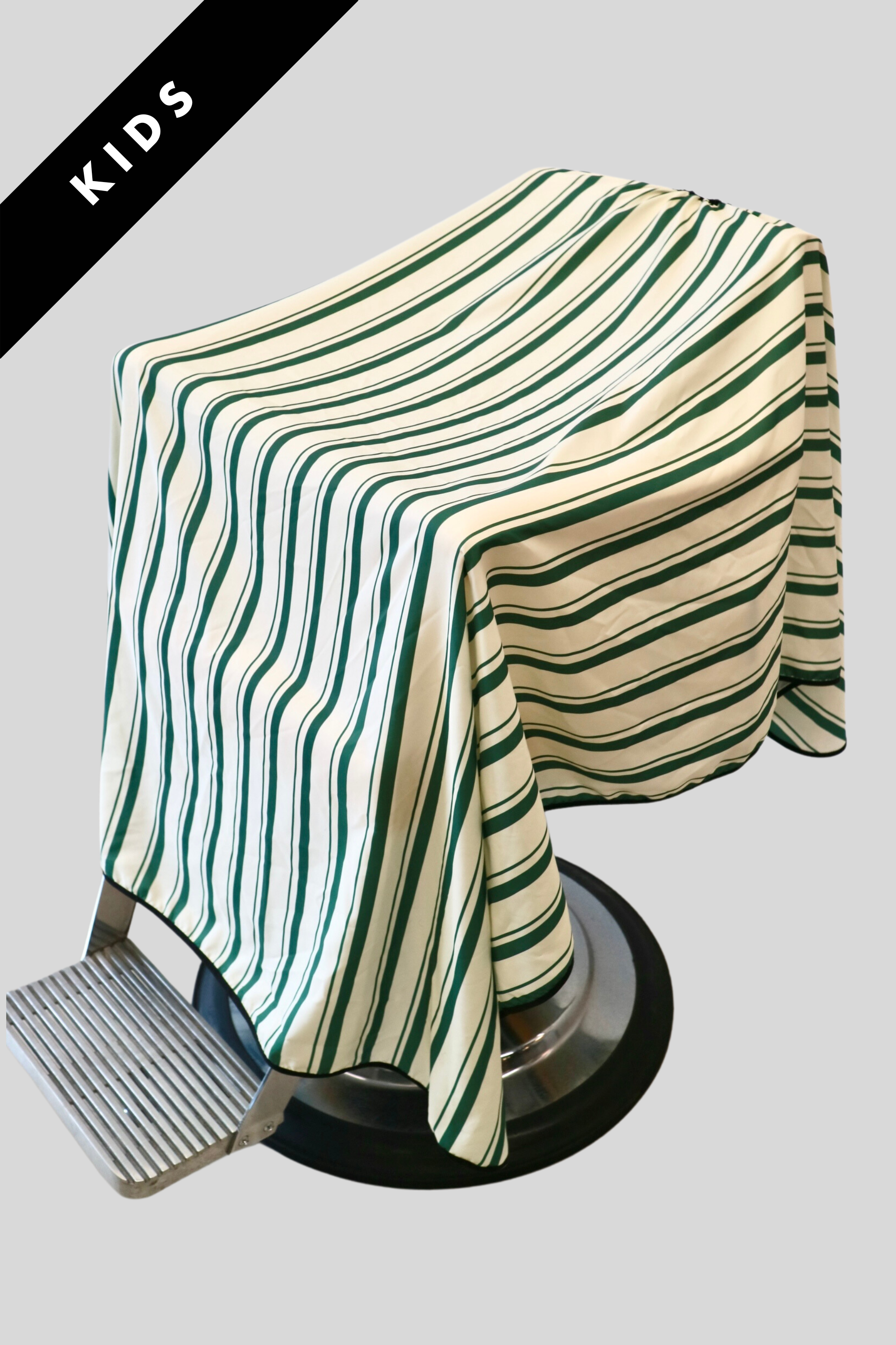 product photo of striped green and cream kids cape. full coverage cape draped on barbershop chair