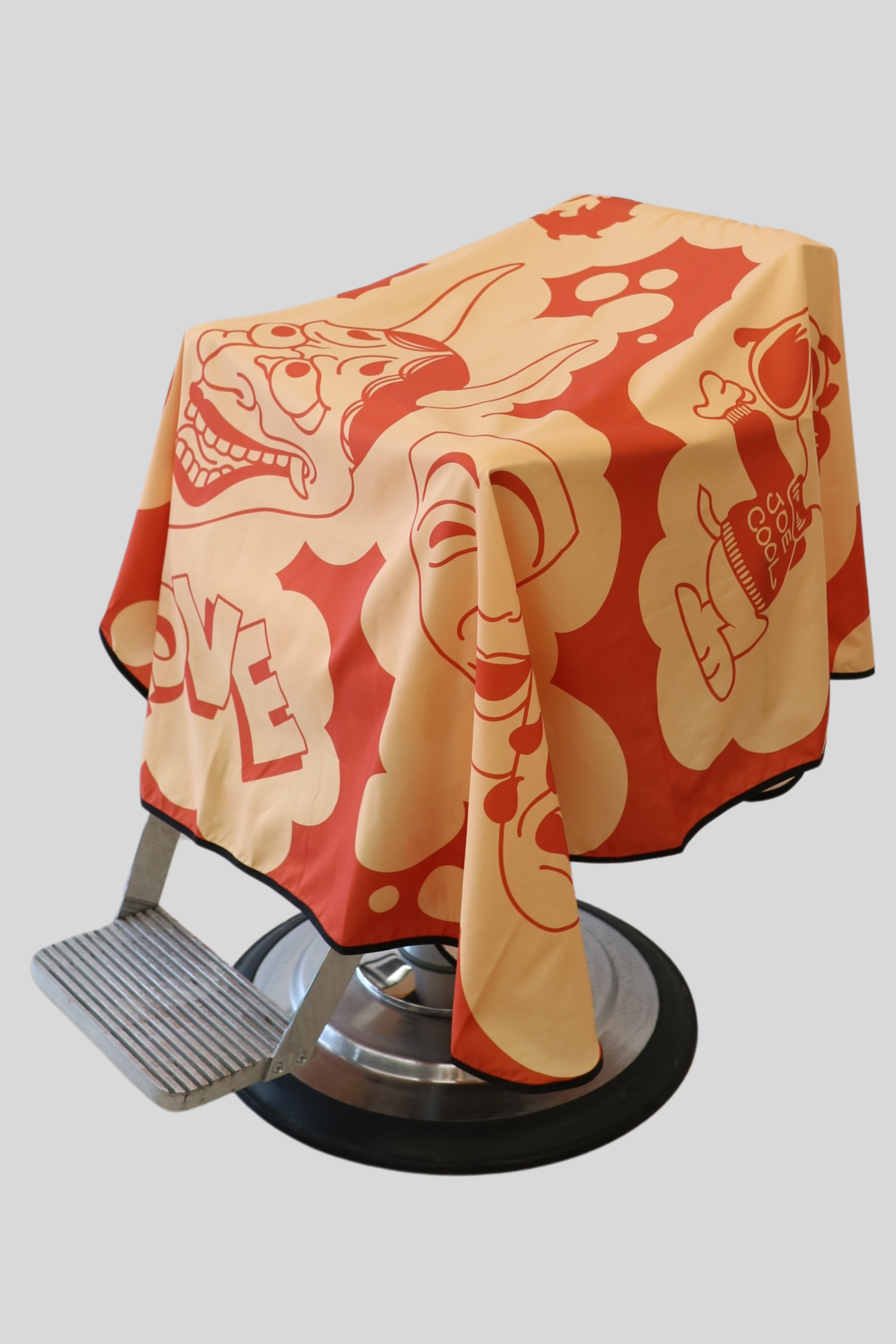 main photo of the orange and yellow barber cutting cape draped on barber chair with cartoon images