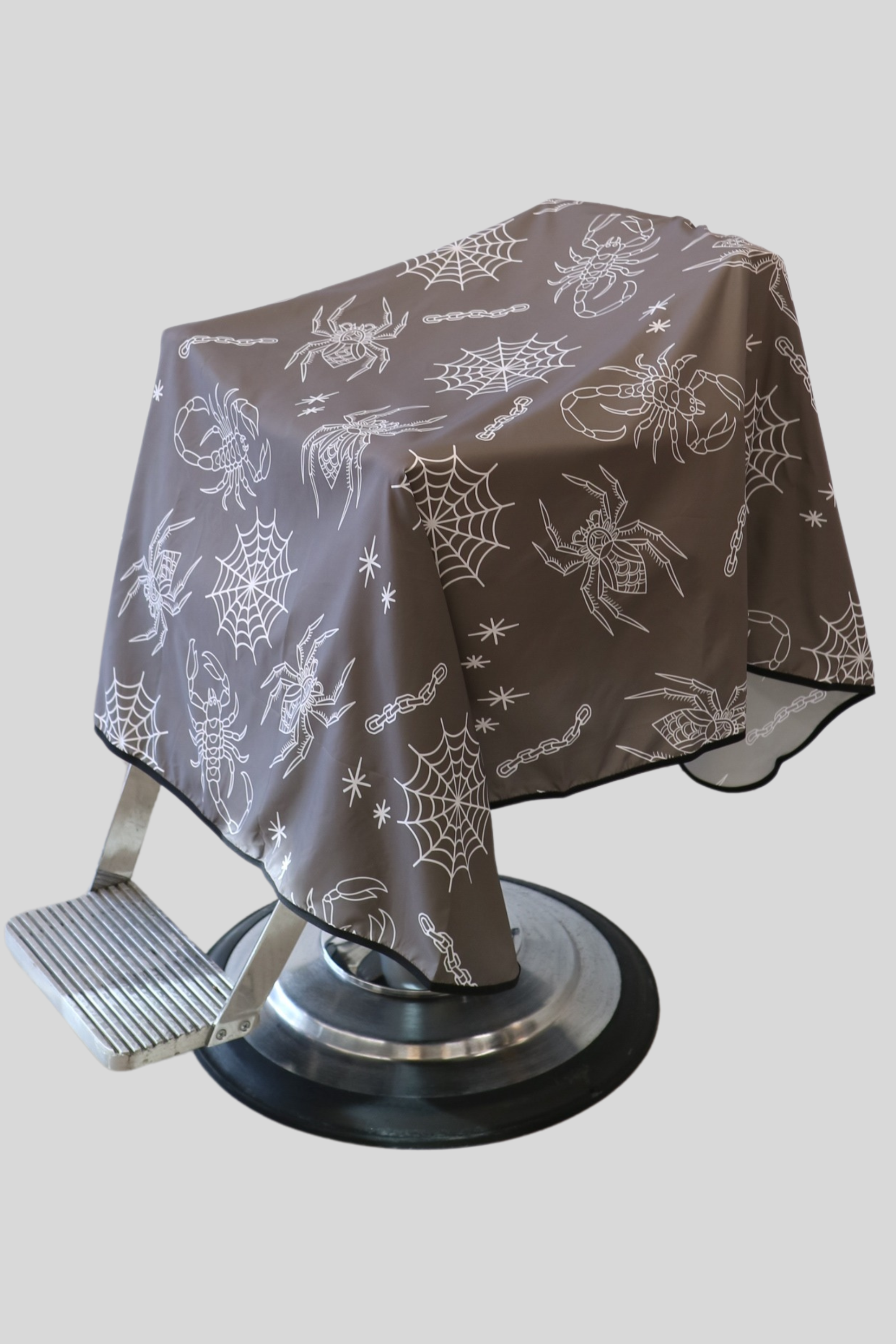 a photo of the clay outback barber cutting cape draped on barber chair. White spiders and webs on a warm clay colored background