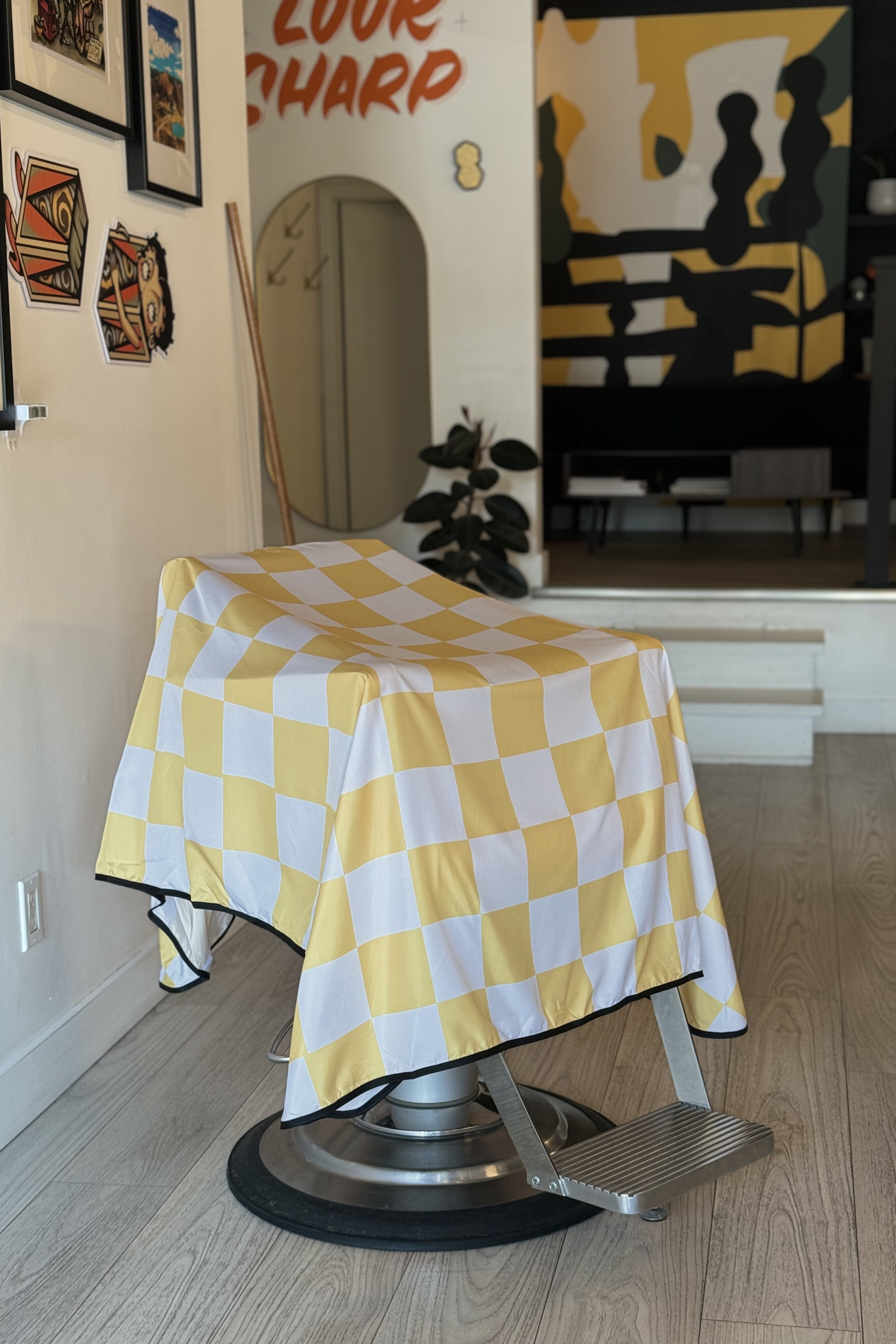 a barber chair inside a barbershop with the yellow rally v2 cutting cape draped on barber chair