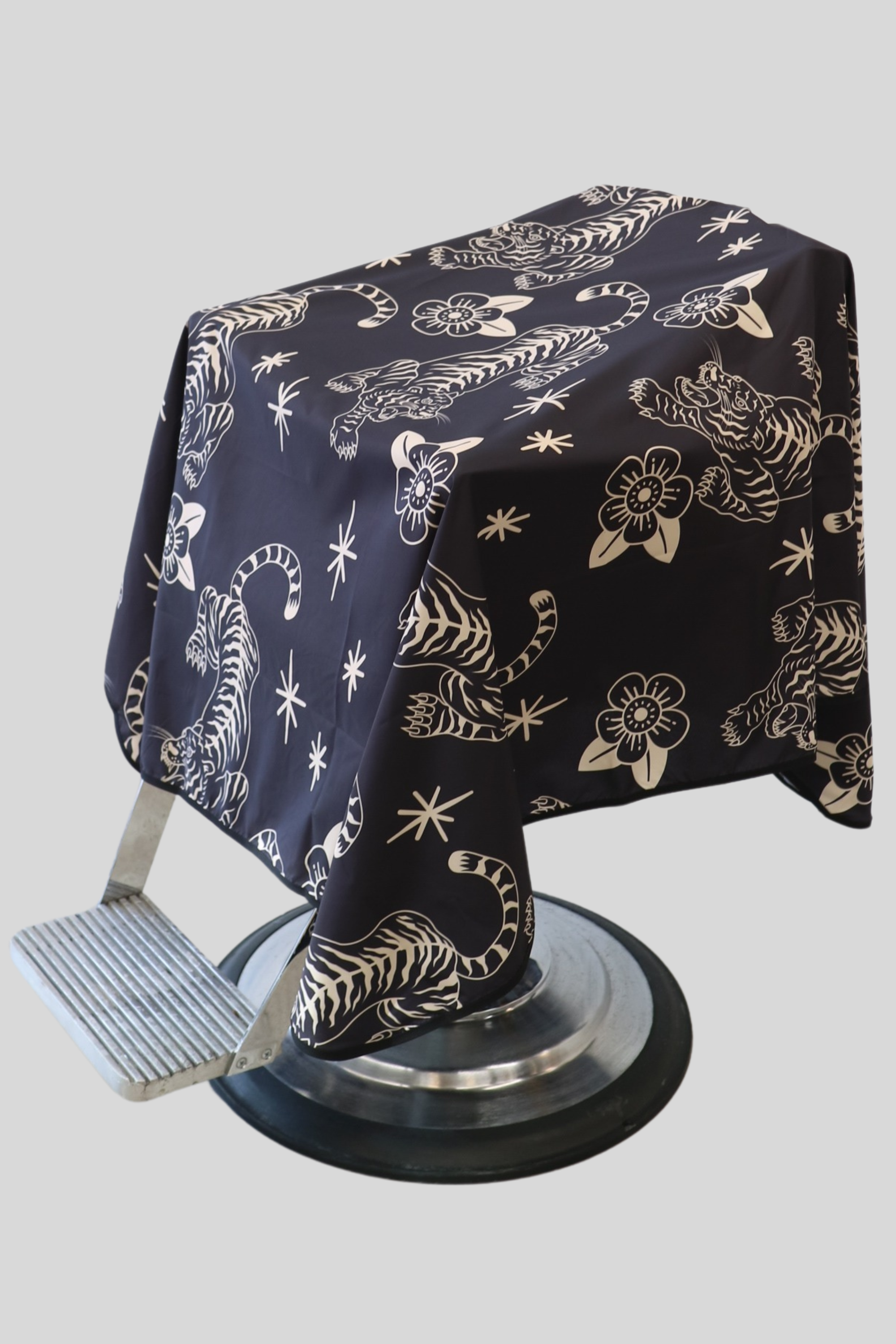 black and cream Tora barber Cape with crawling tiger and floral pattern draped on barber chair